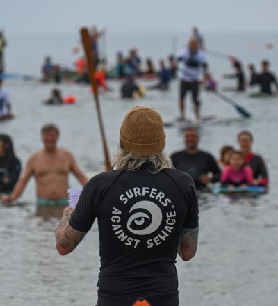 surfer with long hair facing the crowd, surfers against sewage logo on back of his t shirt