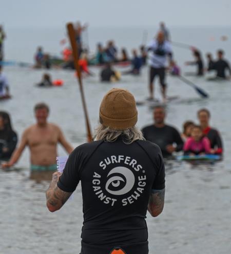 surfer with long hair facing the crowd, surfers against sewage logo on back of his t shirt