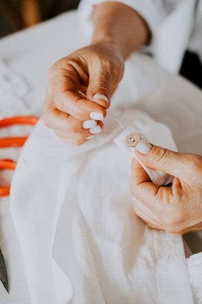 womens hands sewing a button onto a white shirt