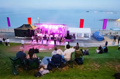 crowds gather on the banks of lister gardens with the seafront stage illuminated below