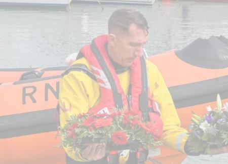 Lyme Regis RNLI crew member with flower wreaths at blessing of the boats ceremony
