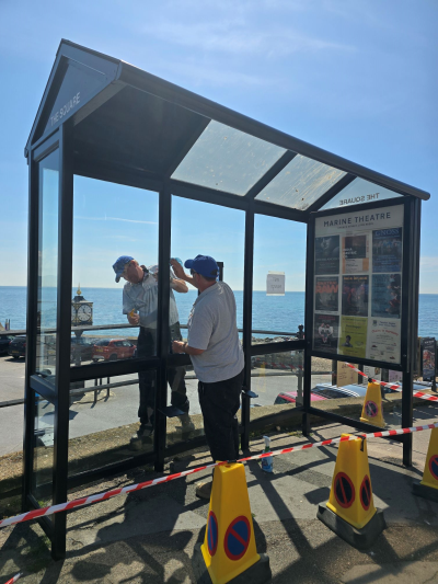 two council workers cleaning and painting the glass bus stop