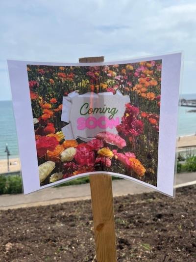 a colourful sign saying coming soon, with bright summer florals, staked into the ground