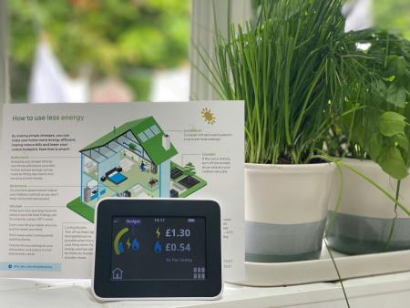 a photo of an in home display electricity meter on a windowsill surrounded by potplants