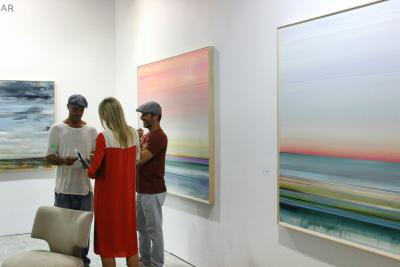 three people in an art gallery looking at paintings on a wall