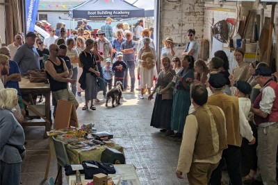 a photo of a group of people stood inside the main workshop of the boat building academy at a previous event 
