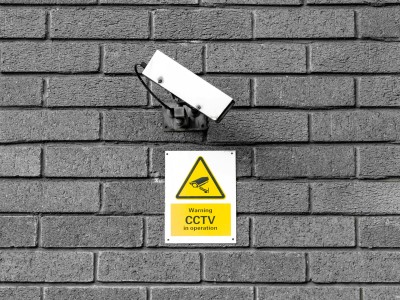 CCTV camera on a brick wall with sign underneath