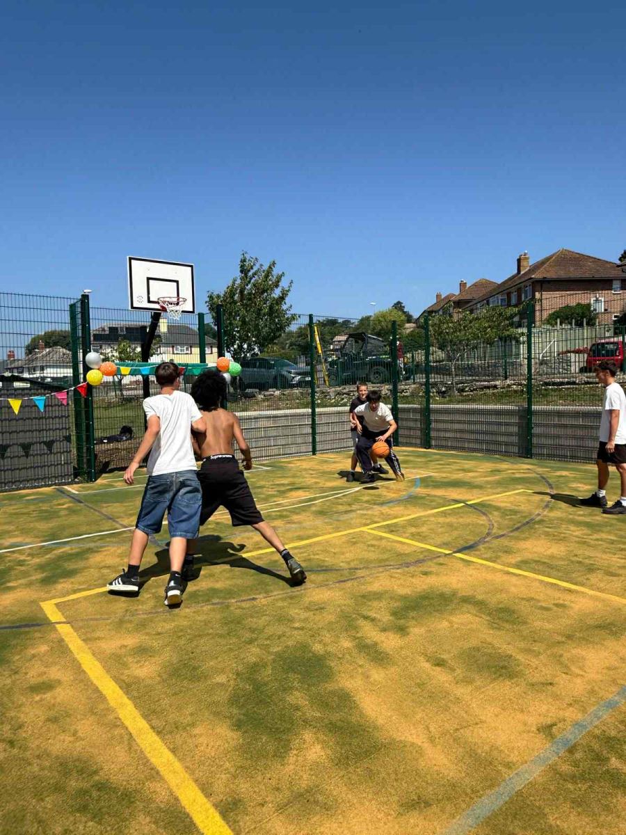 Teenagers play basketball at the multi-use games area in Lyme Regis